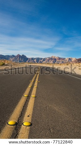 View of a road into the desert toward distant mountains under a nice sky