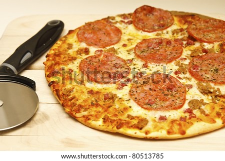 A fresh, hot pepperoni and sausage pizza on a wood cutting board with pizza cutter