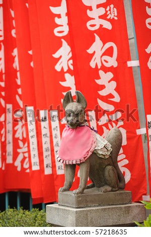 japanese  guardian fox statue made from stone with red flags in front of shrine