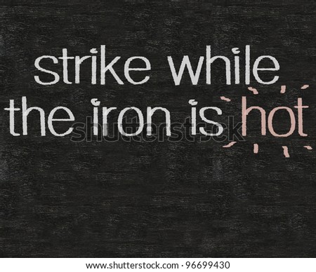 business idioms strike while the iron is hot written on blackboard background