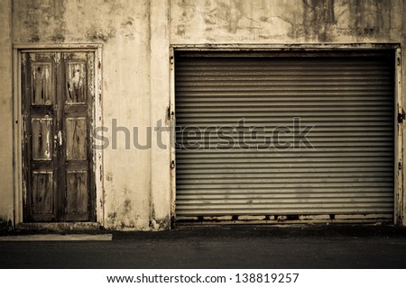Illuminated grunge metallic roller shutter door near wooden door vintage style.