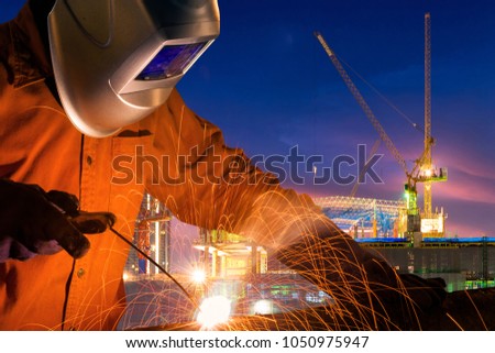 Industrial worker welding steel structure for infrastructure building project with construction site background.