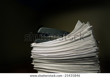 A stapler sits on top of a stack of stapled paper.