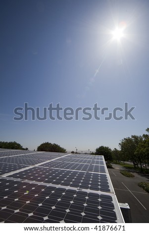 Wide angle shot of solar panels and the sun shining down.