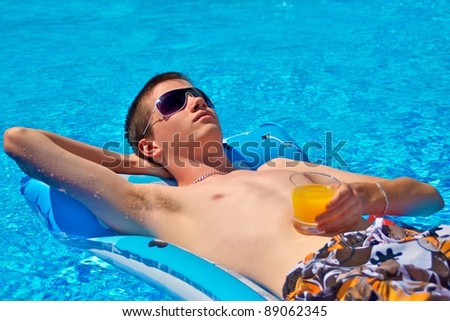 Relaxing teenager lying on a Lilo in a pool looking up with a refreshing drink