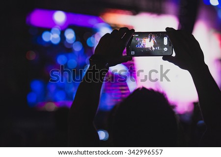 Boy makes photo with His smartphone to a concert to share the moment with friends on social networks, image with copyspace, added vintage effect, blurred effect and grain