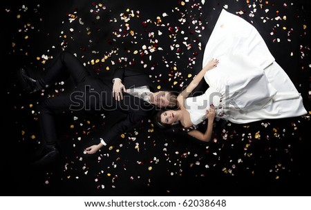 Just married couple lying on black backgruond with flower petals, a lot of copyspace available