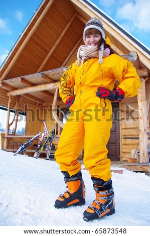 Beautiful, attractive caucasian brunette in yellow skiing outfit ready for skiing. View from the bottom.