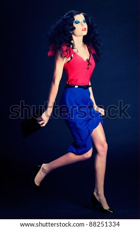 A sexy black headed pin up girl in blue skirt and red shirt on black. Fashion shoot.