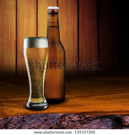 Glass and bottle of cold beer with foam on wood table with wood background