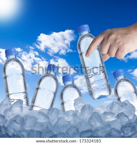 Hand picking up water bottle from ice cubes