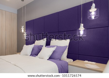 Interior of the room in light colors. Bedroom with bed and lighting in colors of the year 2018, ultra violet.