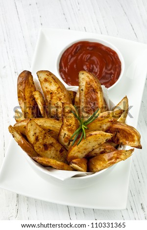 Potato wedges in a bowl, with ketchup and rosemary. Oven baked.