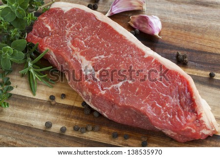 Raw red sirloin steak with fresh herbs, garlic and peppercorns.