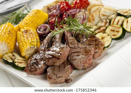 Serving platter of barbecued lamb cutlets and grilled vegetables.