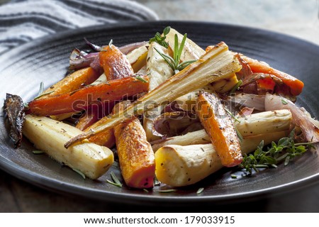 Roasted root vegetables on a black serving platter.  Carrots, parsnips, turnips, red onions, and herbs.