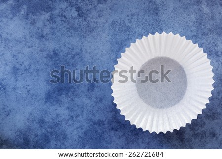 Empty white paper cupcake case over textured blue background.  Overhead view.
