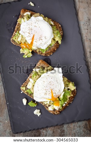 Smashed avocado and feta cheese toast with poached eggs.  Overhead view, on dark slate.