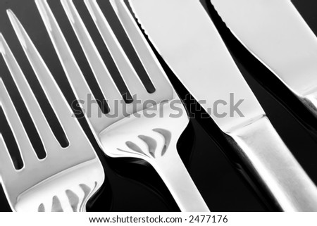 Dinner Knives and Forks Reflected on a Black surface.