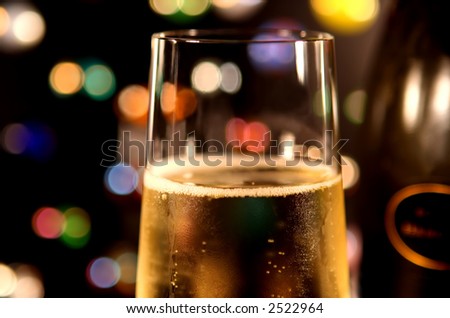 Closeup of a glass of bubbling champagne, against multi-colored lights.  Bottle in background.