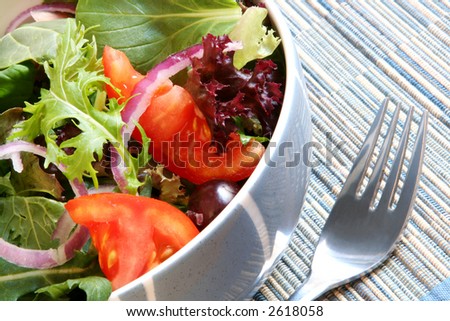A blue bowl of fresh green salad, with mixed lettuce and spinach leaves, tomatoes, spanish red onions, and black olives.