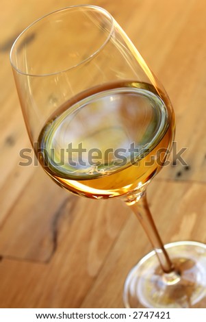 A glowing glass of white wine, in natural light on a rough timber table.