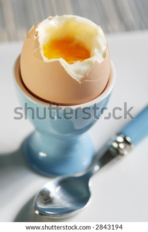 Soft-boiled egg in blue egg cup with matching spoon.