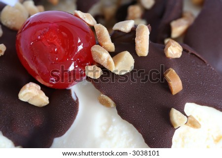 Closeup of a cherry and chopped nuts, on top of a chocolate sundae.