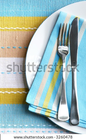 Place setting with silver fork and knife on pastel napkin, and matching placemat.  Vertical view.