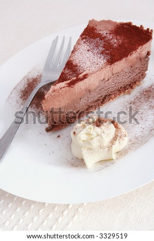 Chocolate mousse cake with fresh whipped cream, on a white plate with cake fork.