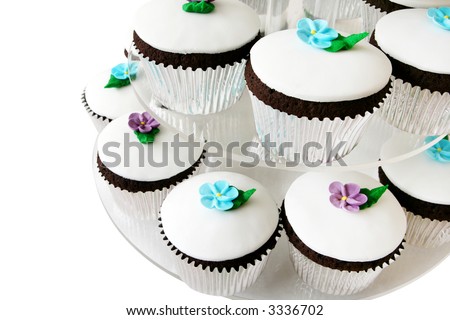 Fancy little cup cakes on a cake stand. Each is iced with royal icing and a flower, in a silver case.