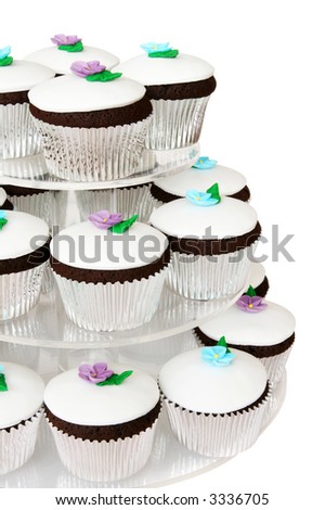 Fancy chocolate cup cakes on a cake stand, each one iced with white icing and a tiny pastel-colored flower.
