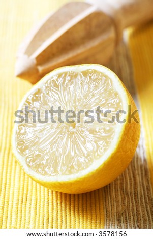 Lemon half on yellow textured mat, with wooden citrus squeezer.