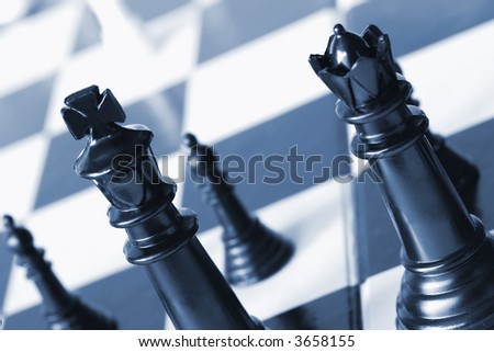 Chess pieces in blue duotone.  Focus on black king and queen.