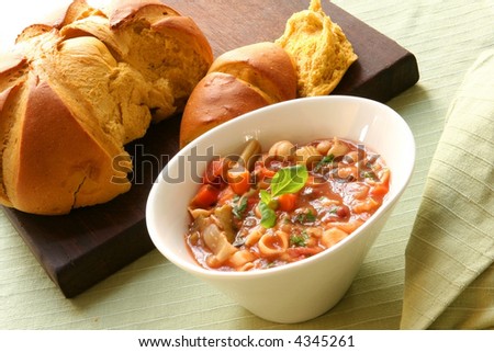Bowl of hearty minestrone pasta and vegetable soup, with fresh pumpkin bread.  A warming meal.