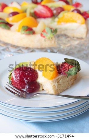 Fruit tart served on a plate with cake fork, with remainder of tart behind.  Shallow depth of field.