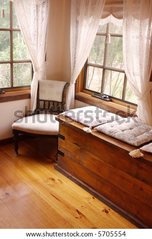 Cozy corner of a Victorian country cottage, with cushioned window seat, and 19th century chair.