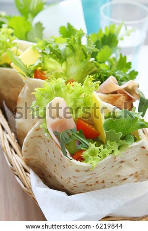 A basket of pita bread pockets filled with ham and salad.  Healthy eating.