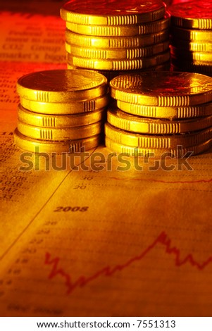 Stacks of gold coins on newspaper finance graph.  Warm tones.
