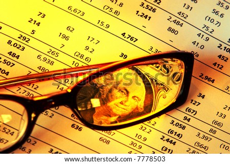 Keeping an eye on the money - US dollar bill viewed through reading glasses on financial info.