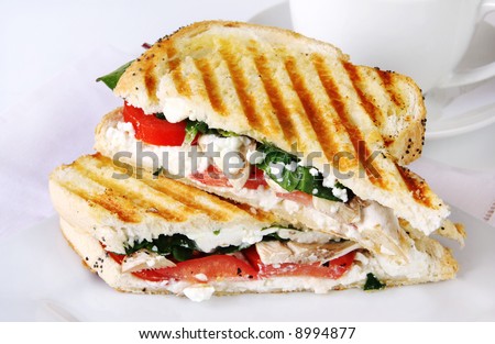 Grilled sandwich or panini, with goat\'s cheese, spinache and tomatoes.  Cup of coffee behind.