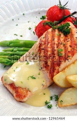 Meal of grilled atlantic salmon with potato wedges, roasted truss tomatoes, and hollandaise sauce.