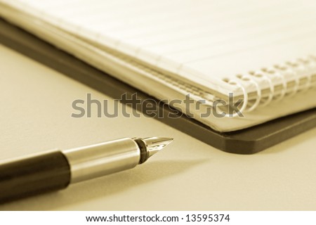 Fountain pen with notepads.  Focus on tip of pen, sepia tone.