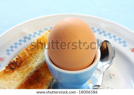 Boiled egg in an egg cup, ready for cracking open.  Accompanied by toast fingers.