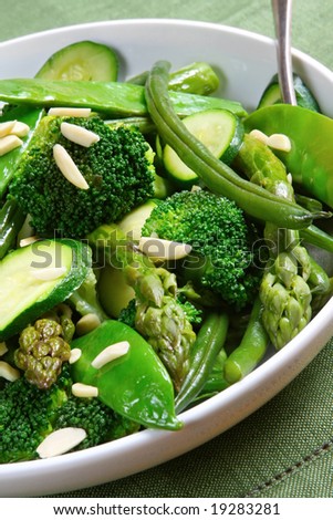 Serving bowl of mixed green vegetables, topped with toasted almonds.  Delicious healthy eating.