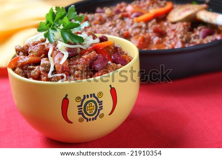 Bowl of chili with beans, with cooking pan behind.  Delicious chili con carne.