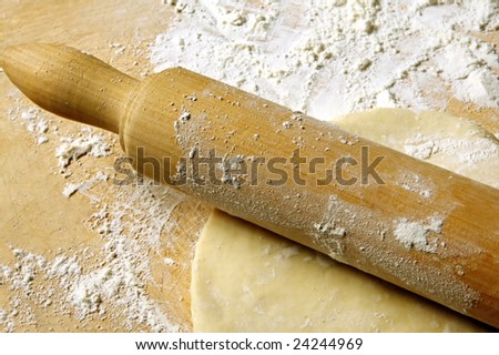 Old rolling pin rolling out pastry, on flour-covered board.