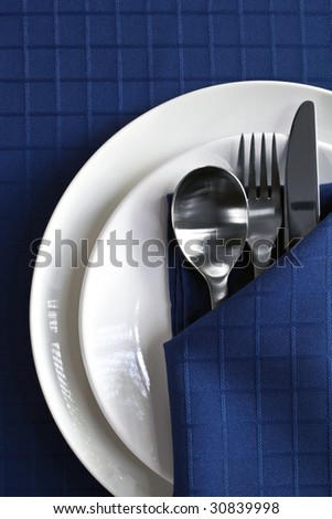 Place setting with plates, silverware, and navy blue napery.