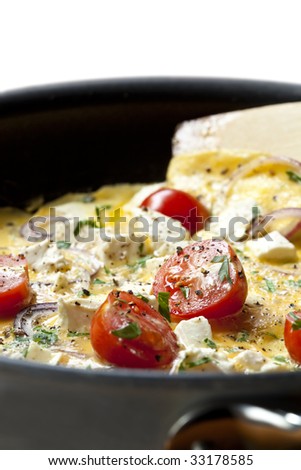 Cooking omelet in a pan, ready to serve.  With Cherry tomatoes, red onion, goat\'s cheese and parsley.  Shallow DOF.