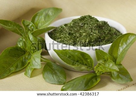 Basil pesto in a small bowl, with fresh basil leaves.  Soft focus.